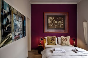 A hotel room with a bed, two bedside tables, a nightstand, and artwork on the walls.