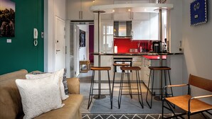 Een compacte leefruimte met een kitchenette, een eethoek met krukken en een bank met gestreepte kussens.