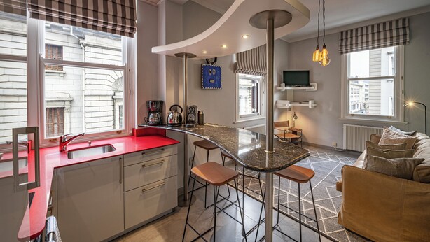 Een moderne keuken met een rood aanrecht, barstoelen, een koffieapparaat en een aan de muur bevestigde televisie.