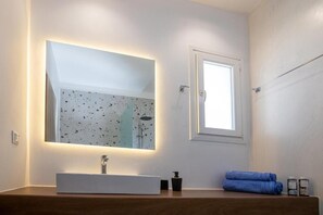 Un bagno con un grande specchio, un lavandino bianco, un asciugamano e una finestra.