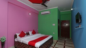 A hotel room with a bed, a ceiling fan, an air conditioning unit, a TV, and a door. - Ugte Hotel (Rishikesh)