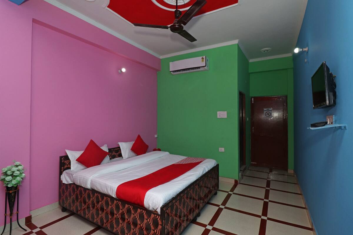 A hotel room with a bed, a ceiling fan, an air conditioning unit, a TV, and a door.