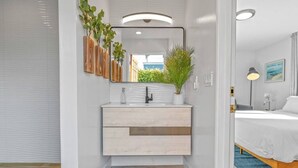 Een moderne badkamer met een witte wastafel, een spiegel en een plant in een pot.