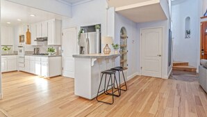 Een ruime keuken met witte kasten, een centraal kookeiland met krukken, en uitzicht op de woonkamer.