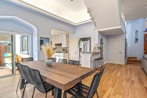 A spacious dining area with a wooden table and chairs, a vase with dried plants, and a view of the kitchen and outdoor patio. - Oceanview Family Playground (Santa Cruz)