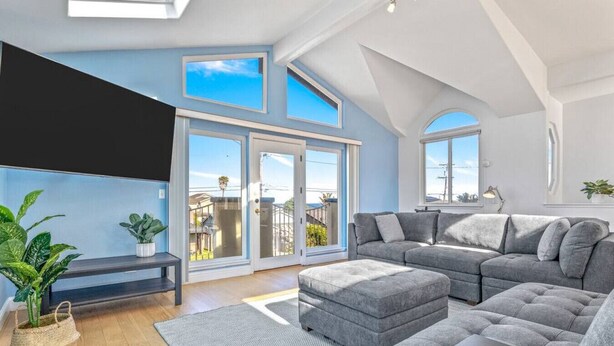 Een ruime woonkamer met een grijze modulaire bank, een flatscreen televisie aan de wand en een grote schuifpui naar een balkon.