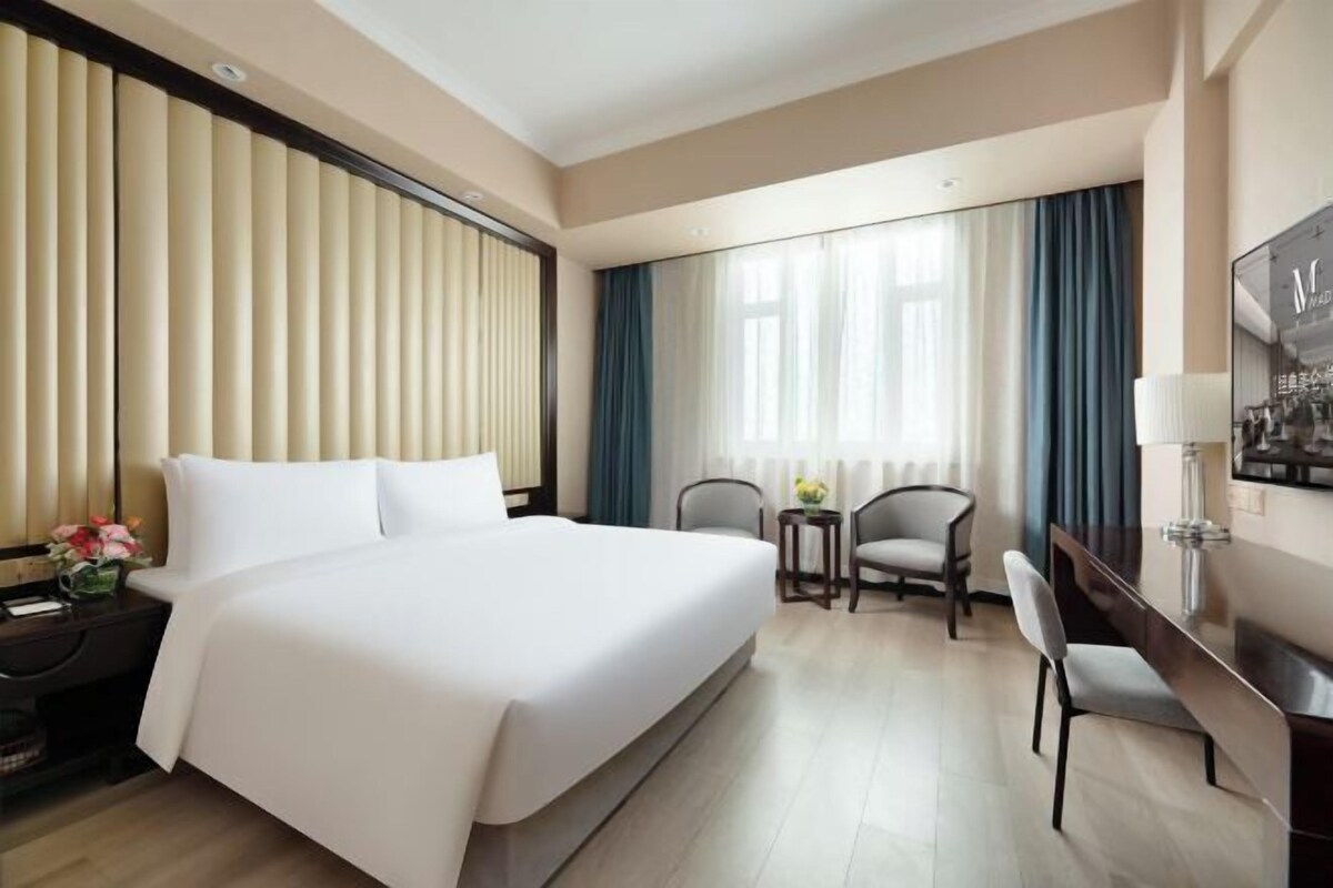 Habitación de hotel con una cama grande, dos sillones, un escritorio y una ventana con cortinas.