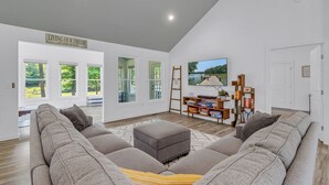 Ein geräumiges Wohnzimmer mit einem großen, grauen Ecksofa, einer Holzleiter und einem Bücherregal.