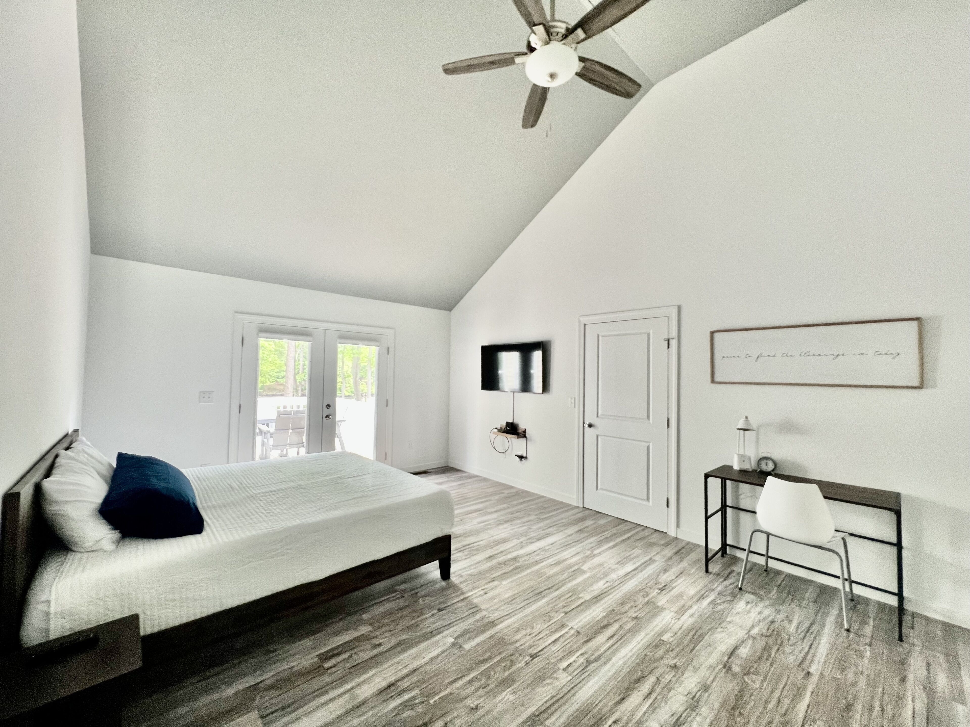 A bedroom with a bed, a desk, a chair, a ceiling fan, and a TV.