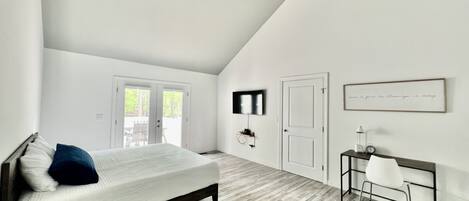 A bedroom with a bed, a desk, a chair, a ceiling fan, and a TV.