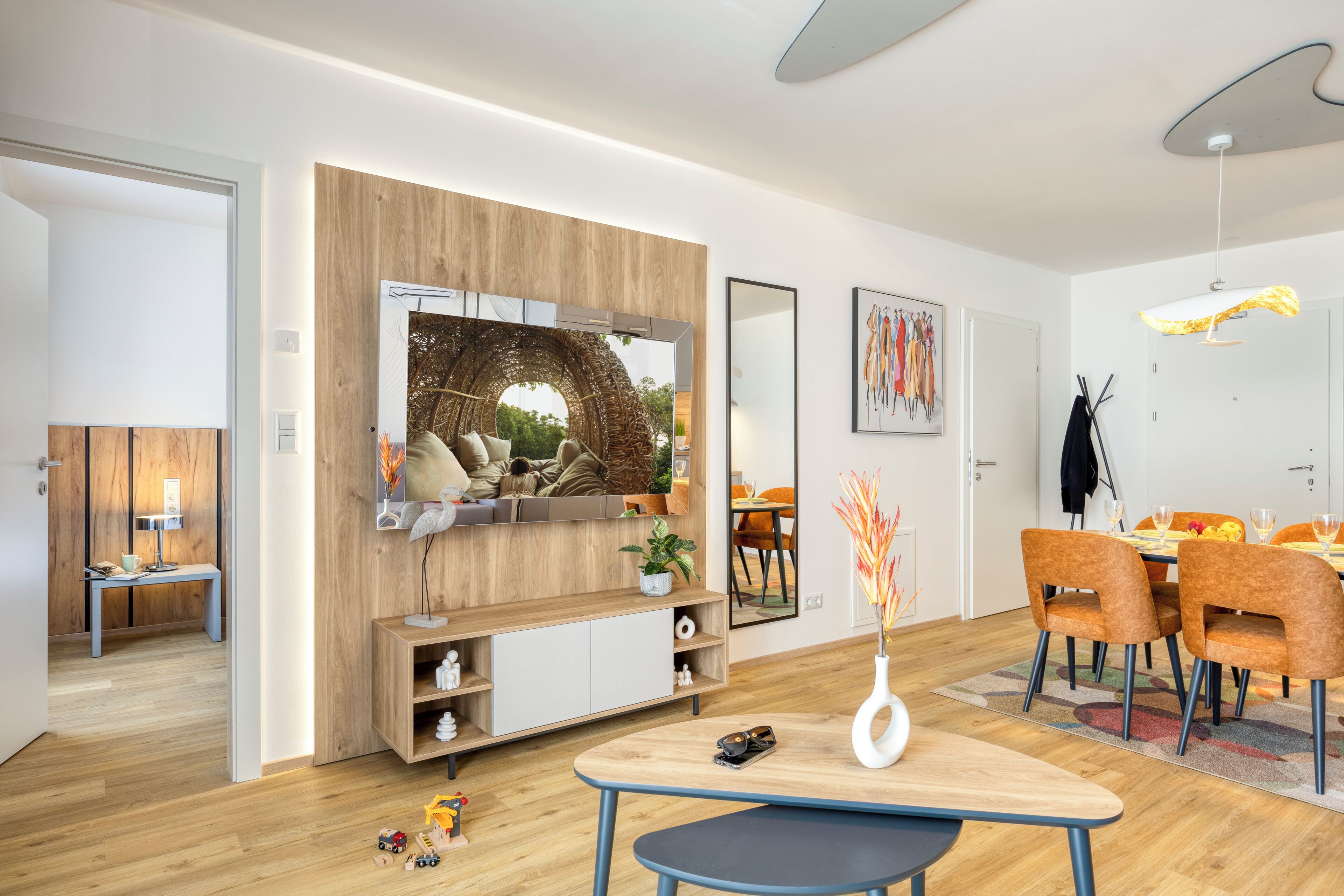 A modern living room with a TV, wooden panel wall, dining area with chairs, and a table.