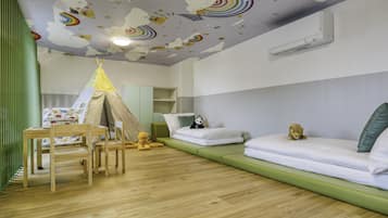 Ein Kinderzimmer mit Holzboden, einem grünen Sofa, einem weißen Bett, einem Spielzelt und einem Holztisch mit Stühlen.