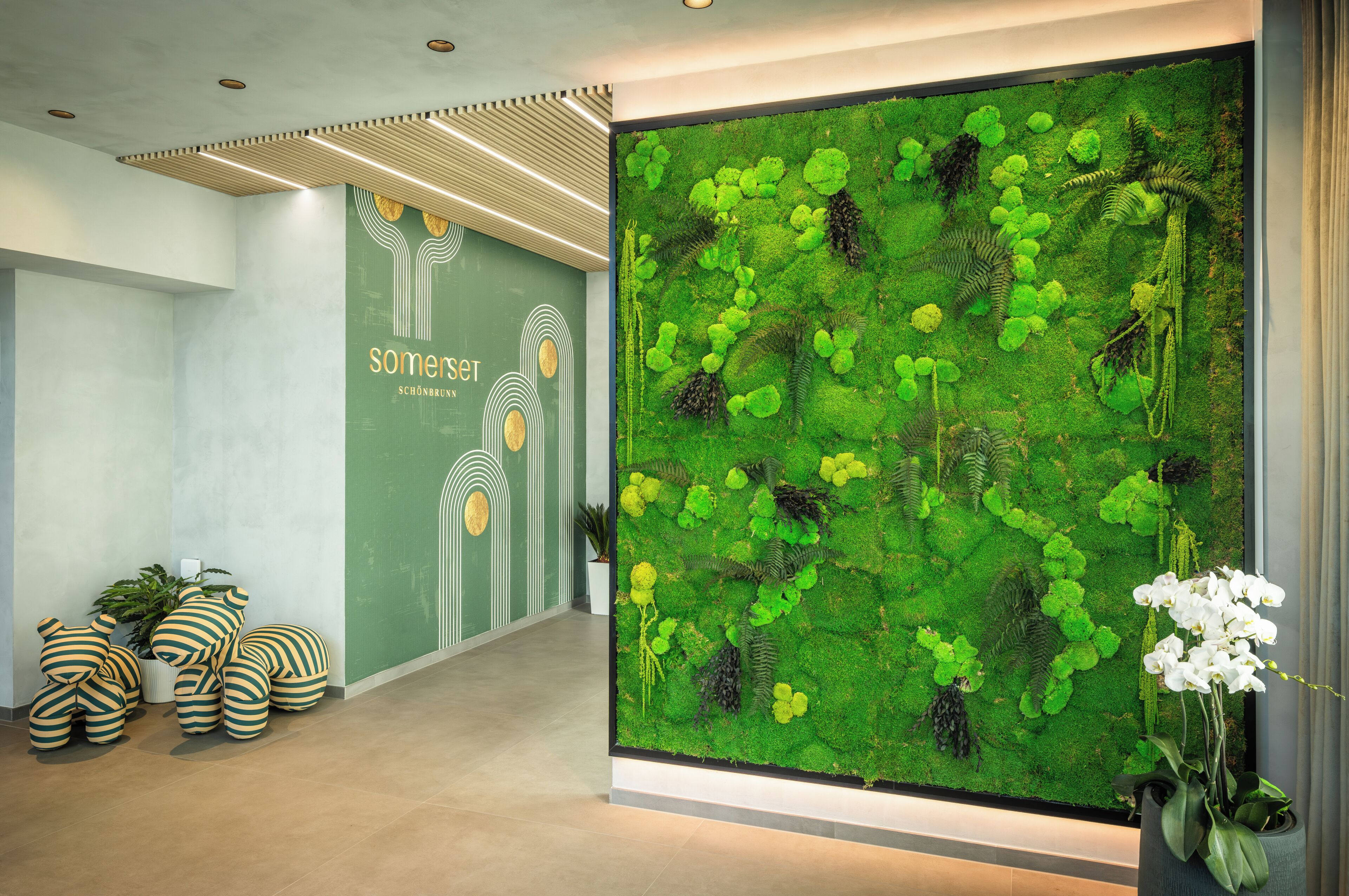 A reception area with a green moss wall, striped cushions, and a logo on the wall.
