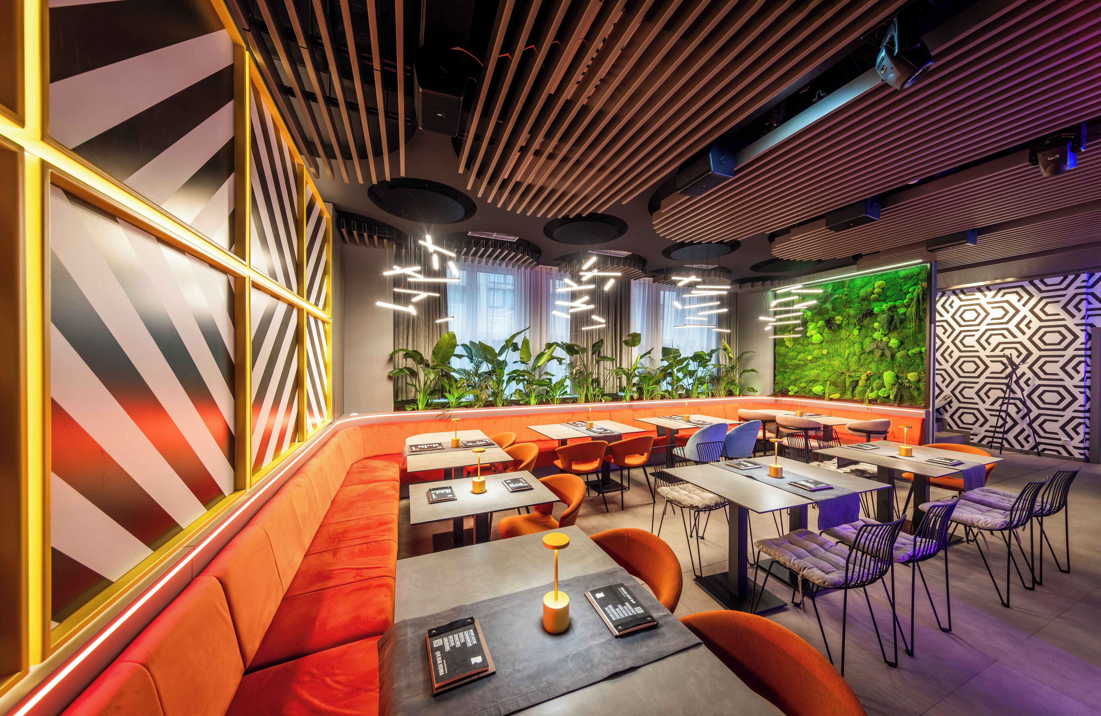 Un restaurante moderno con diversas opciones de asientos, como boxes y mesas, una pared verde con plantas, e iluminación contemporánea.