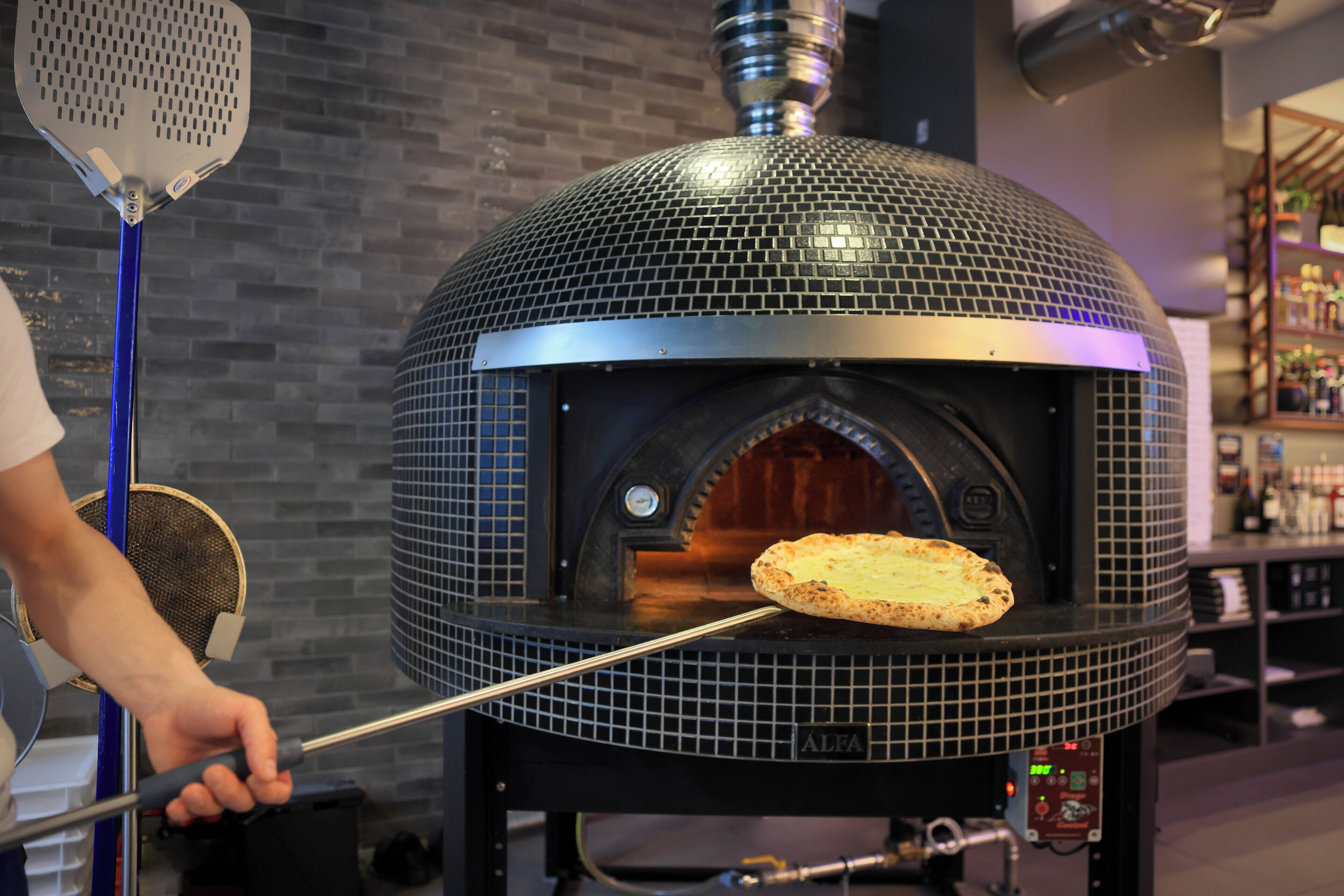 Un muro de ladrillo y un horno de pizza con una pizza que se está introduciendo dentro.