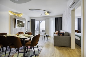 A modern living room with a dining area, featuring a sofa, chairs, a dining table, and a large window with curtains.