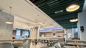 A modern restaurant interior with round tables, grey chairs, and a bar area with shelves of bottles.