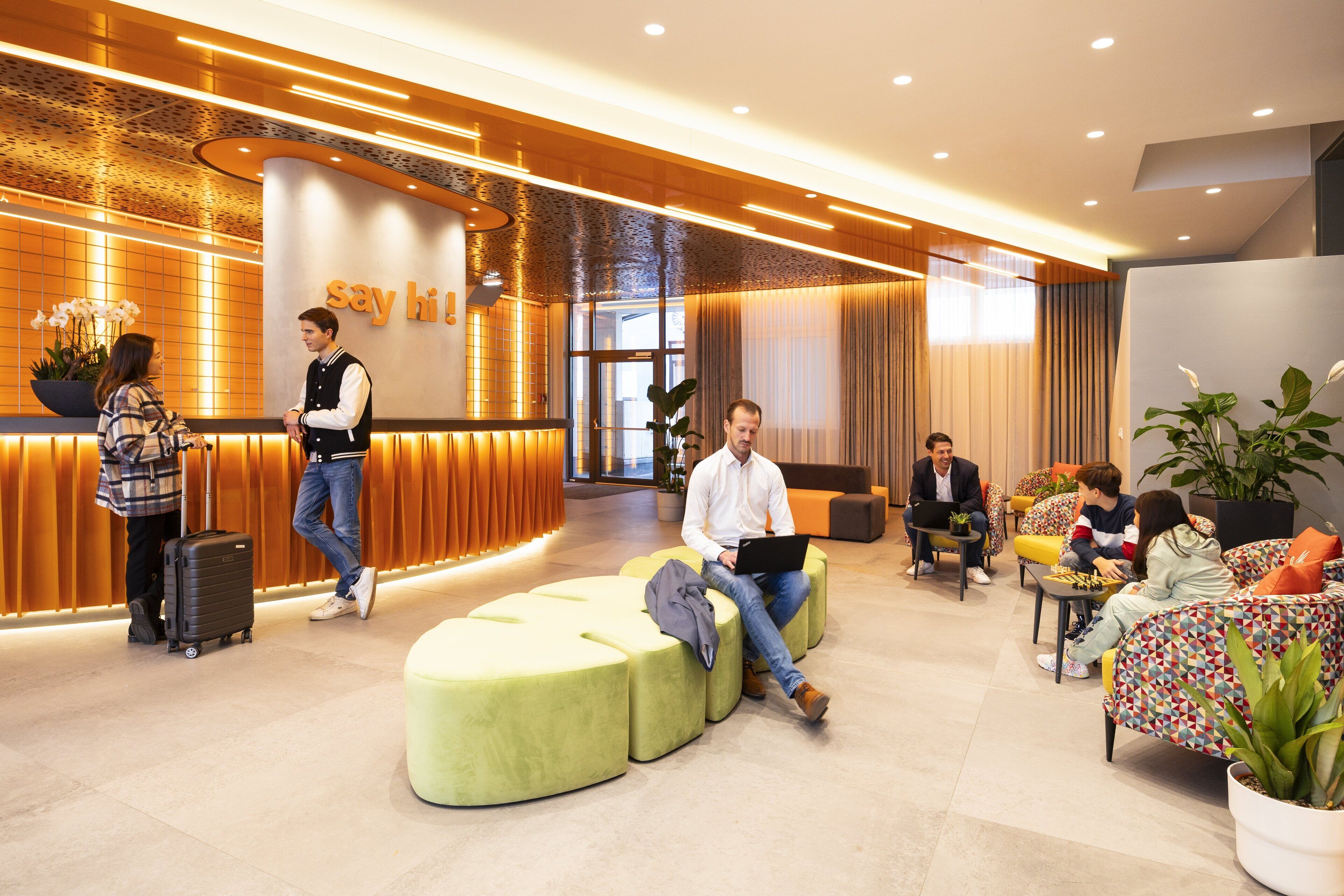 Een moderne lobby met een receptiebalie, zitgedeeltes en plantenbakken.