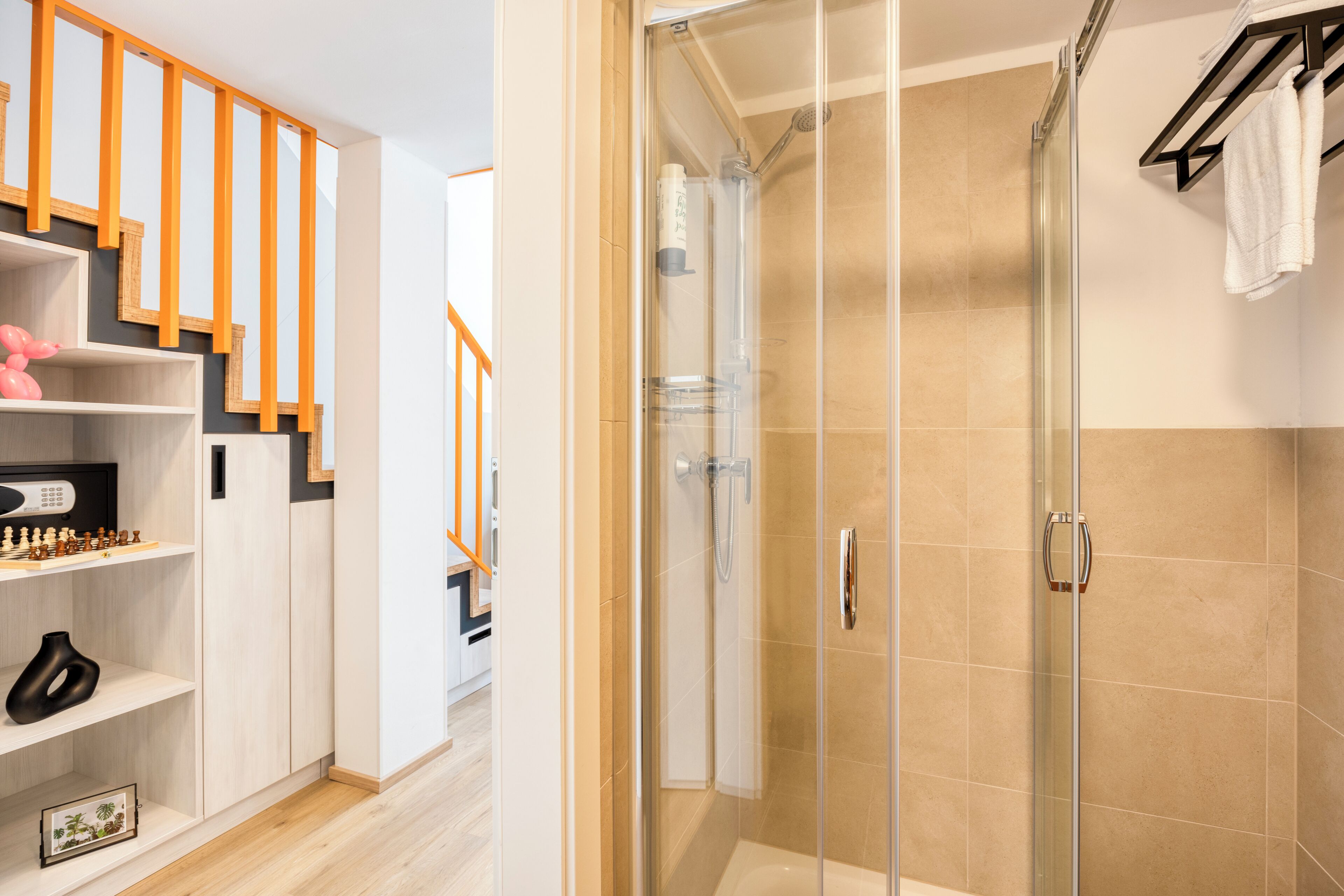 A modern bathroom with a glass-enclosed shower, a white bathtub, and a wooden staircase.