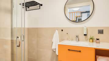 Een moderne badkamer met een glazen douchecabine, een ronde spiegel, een witte wastafel en een oranje badkamermeubel.