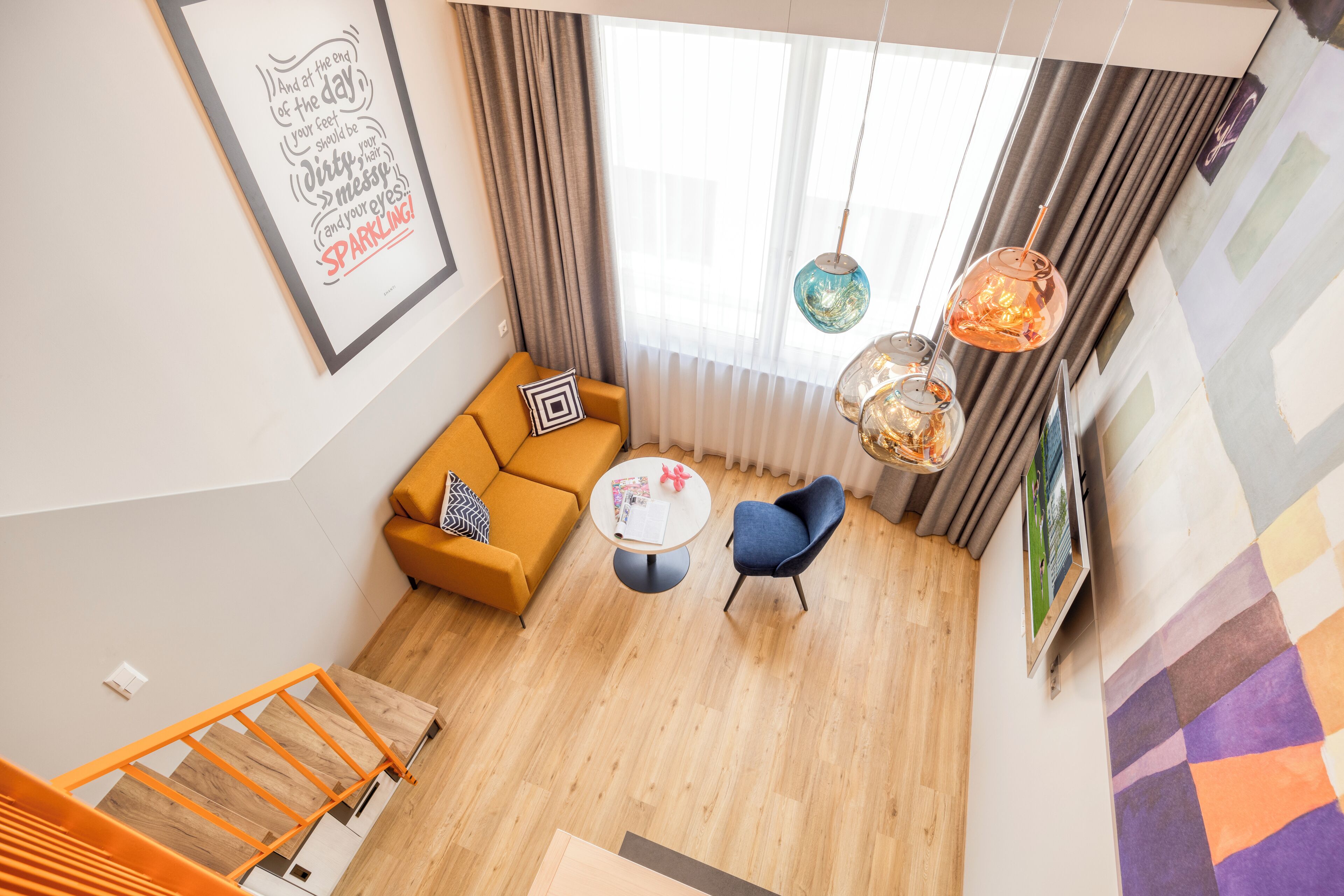 A modern living room with a sofa, a chair, a coffee table, and a staircase with orange railings.