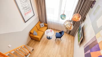 A modern living room with a sofa, a chair, a coffee table, and a staircase with orange railings.