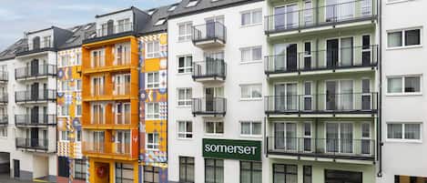 Una hilera de edificios residenciales de varios pisos con balcones, una calle delante y un cielo despejado.