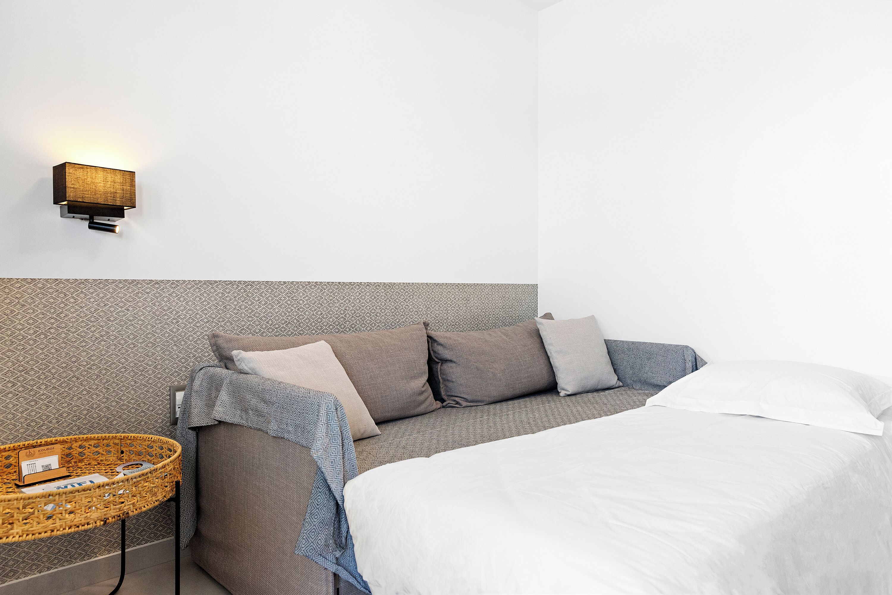 A neatly made bed with a white comforter, a grey headboard, and a wall-mounted light fixture.