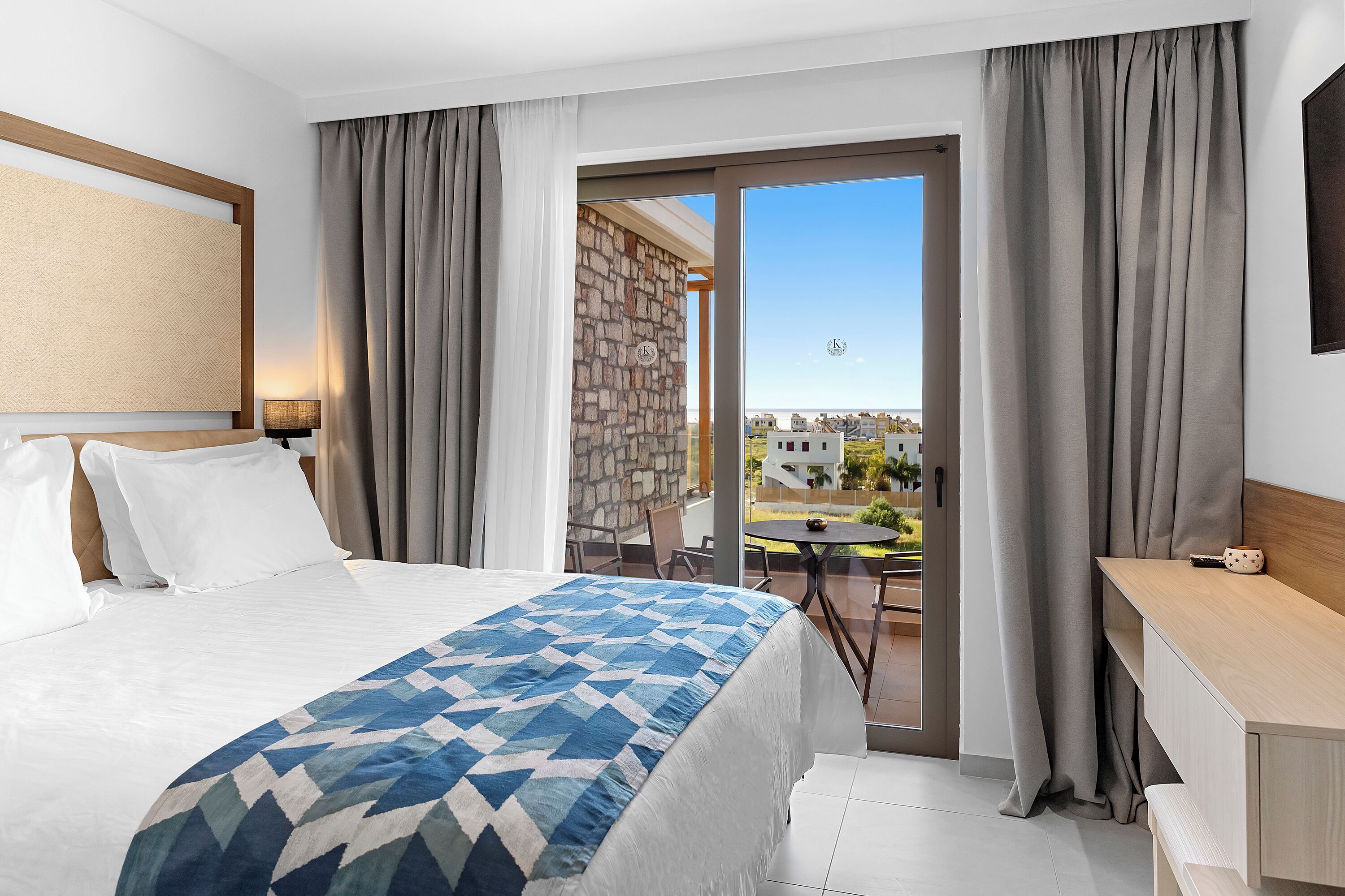 Een hotelkamer met een bed, een bureau en een balkon met uitzicht op gebouwen.