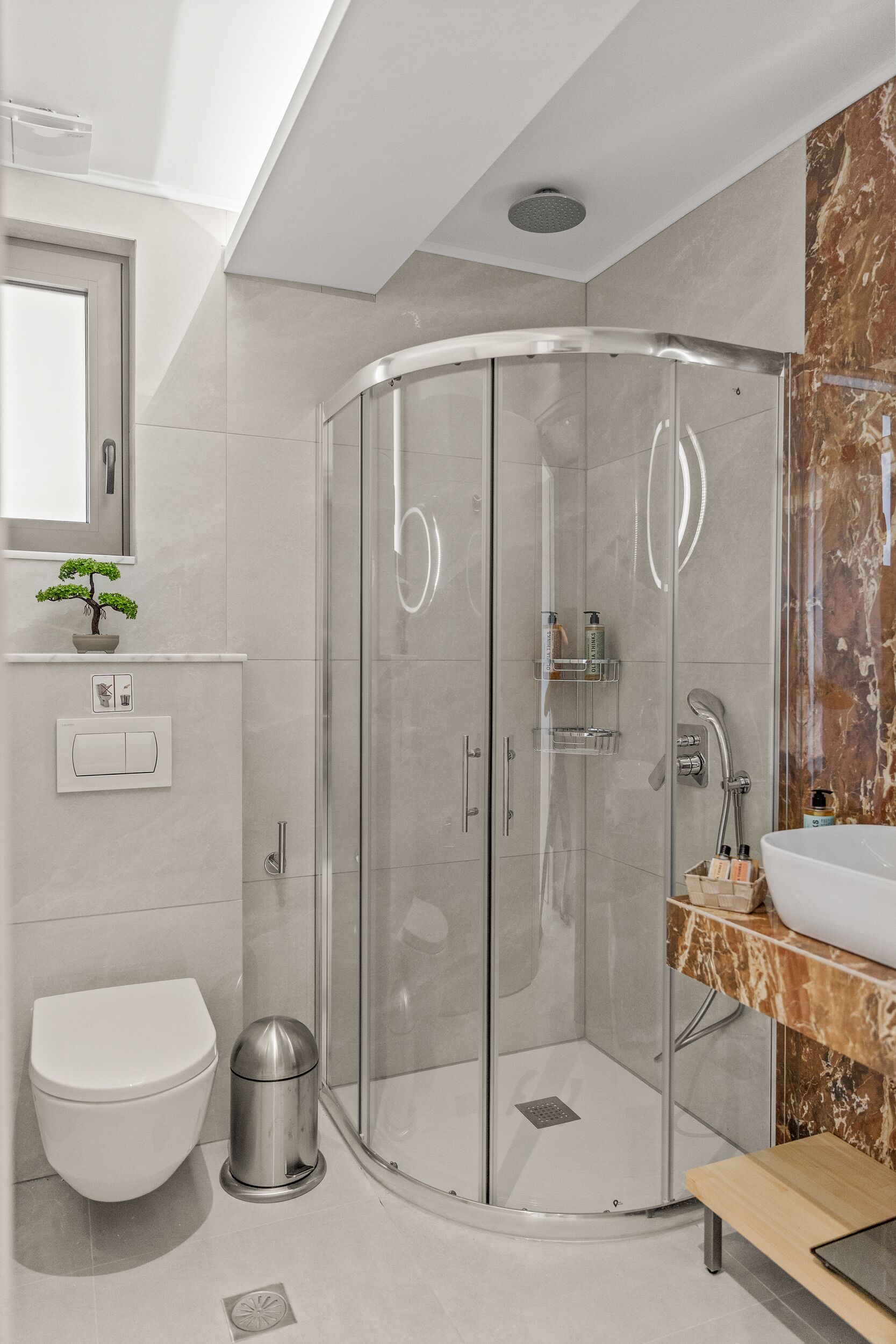 A modern bathroom with a glass-enclosed shower, a white toilet, and a marble sink vanity.