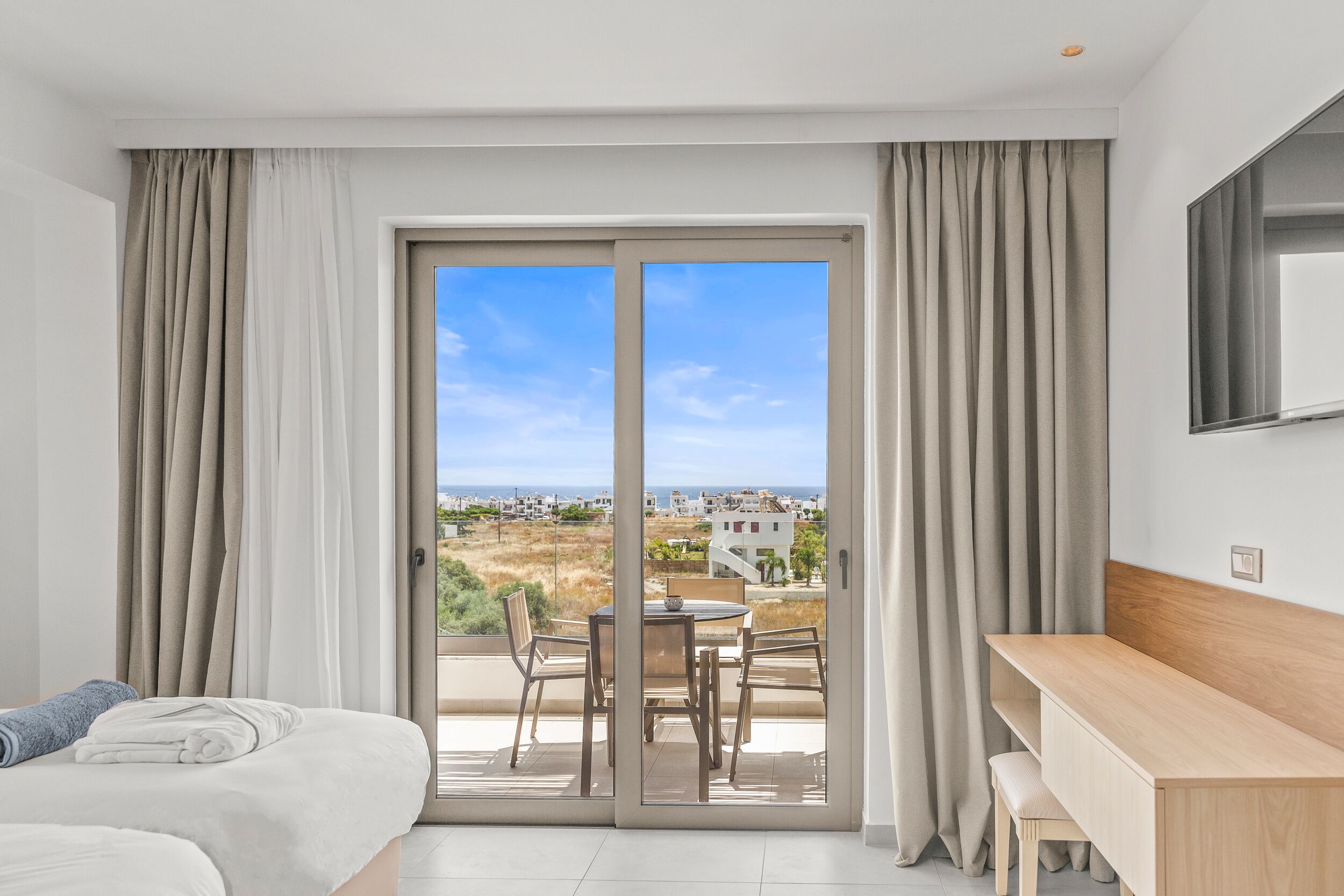 Una habitación de hotel moderna con balcón, cama, escritorio y vistas a la ciudad.