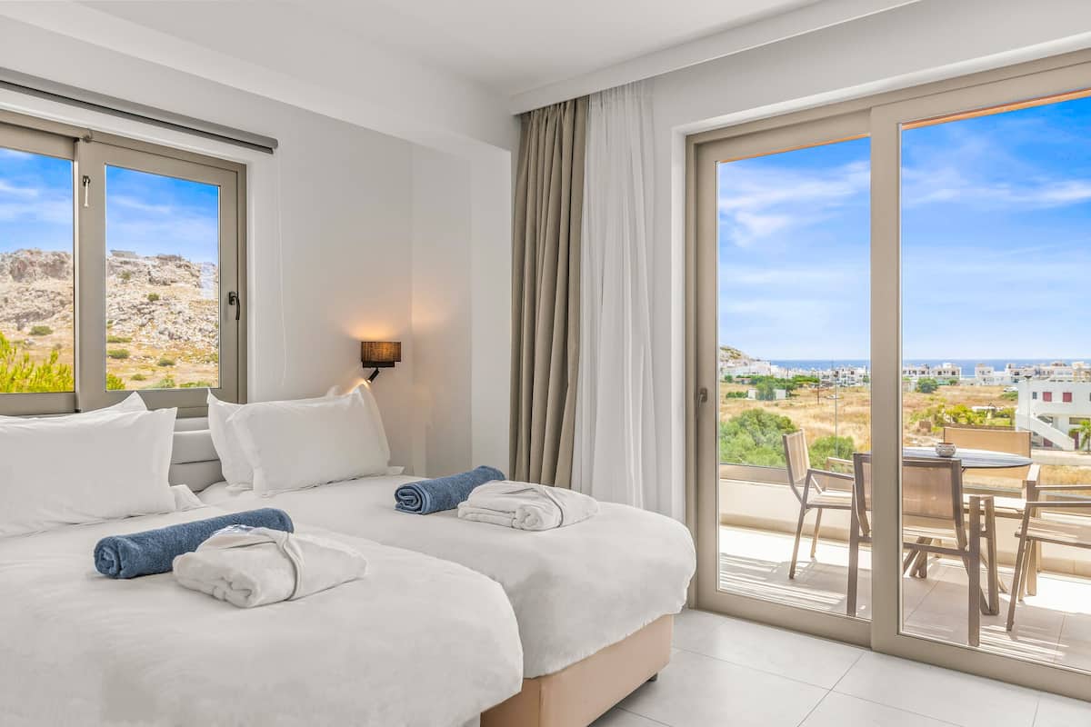 A hotel room with two beds, a balcony with a table and chairs, and a view of the landscape.