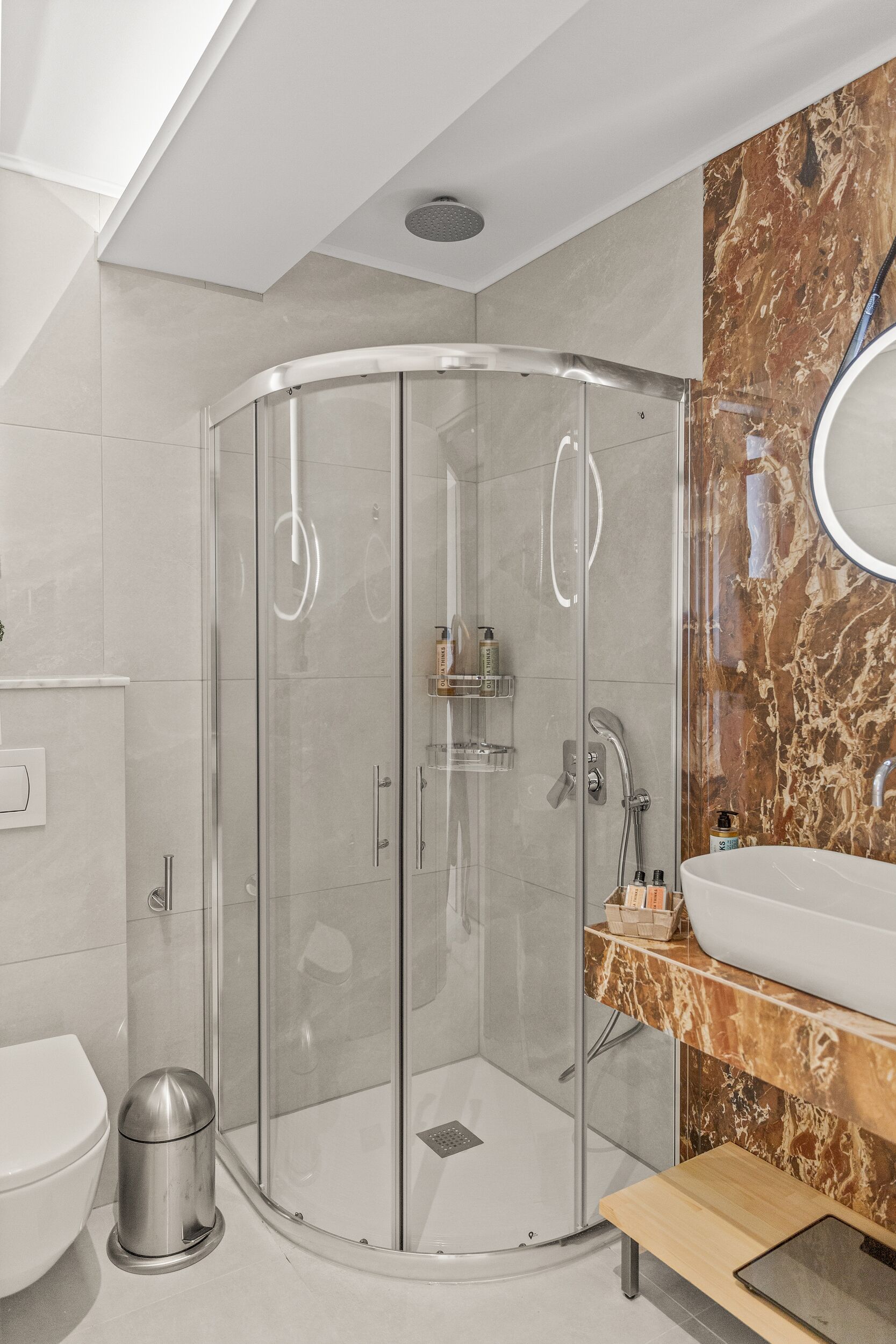 A modern bathroom with a glass-enclosed shower, a marble vanity, and a white sink.