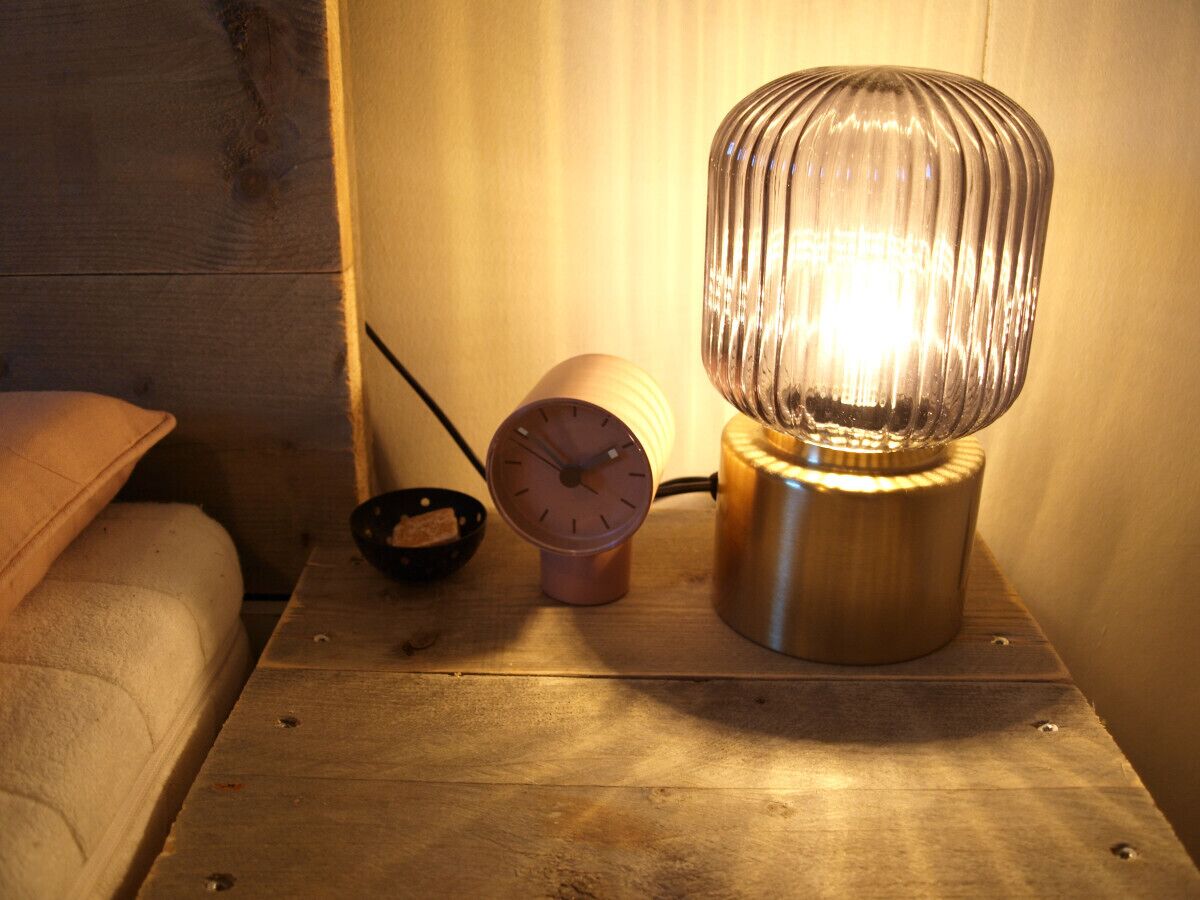 A wooden nightstand with a metallic lamp, a clock, and a small bowl.