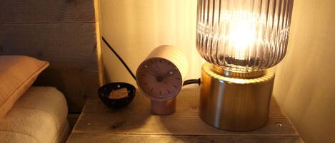 A wooden nightstand with a metallic lamp, a clock, and a small bowl.