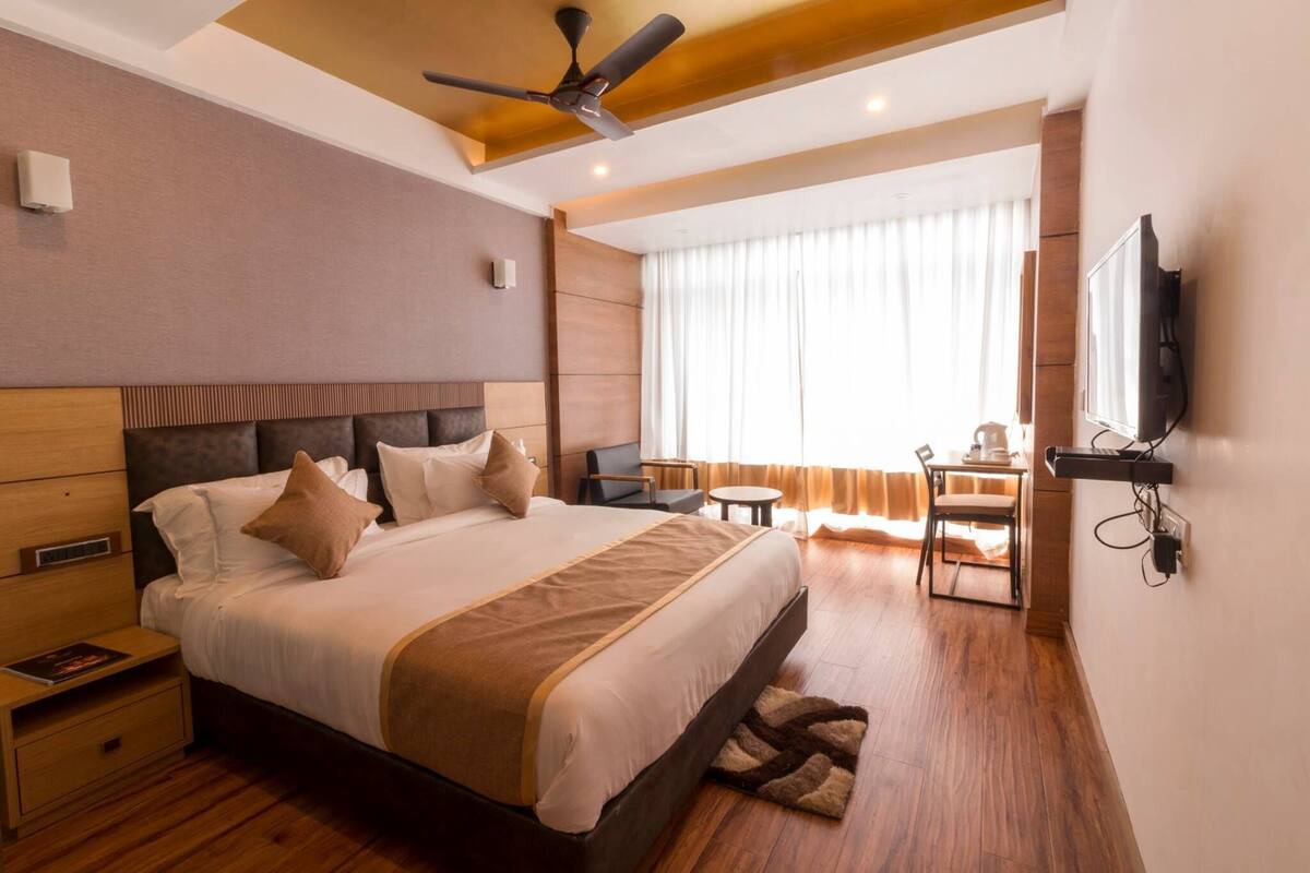 Une chambre d’hôtel avec un grand lit, un bureau, une chaise, une télévision et un ventilateur de plafond.