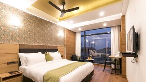 Une chambre d’hôtel moderne dotée d’un grand lit, d’un ventilateur de plafond, d’un téléviseur fixé au mur et offrant une vue sur la ville grâce à de grandes fenêtres.