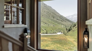 A window with a view of a mountainous landscape, including a winding road and scattered buildings. - Chalet Cecilia by MYALPS (Soelden)
