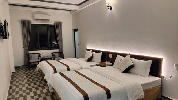 Ein Hotelzimmer mit zwei Betten, kariertem Boden, einem Schreibtisch mit Stuhl und einem Fenster mit Vorhängen.