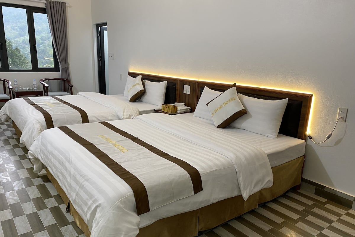 Quarto de hotel com duas camas, piso xadrez e vista para o verde pela janela.