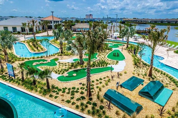 A golf course with multiple putting greens, a swimming pool, and palm trees.