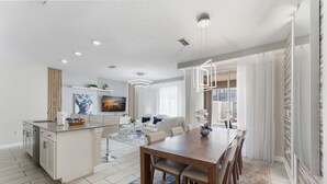 A modern kitchen with a central island, a dining area with a wooden table and chairs, and a living space with a sofa and a TV.