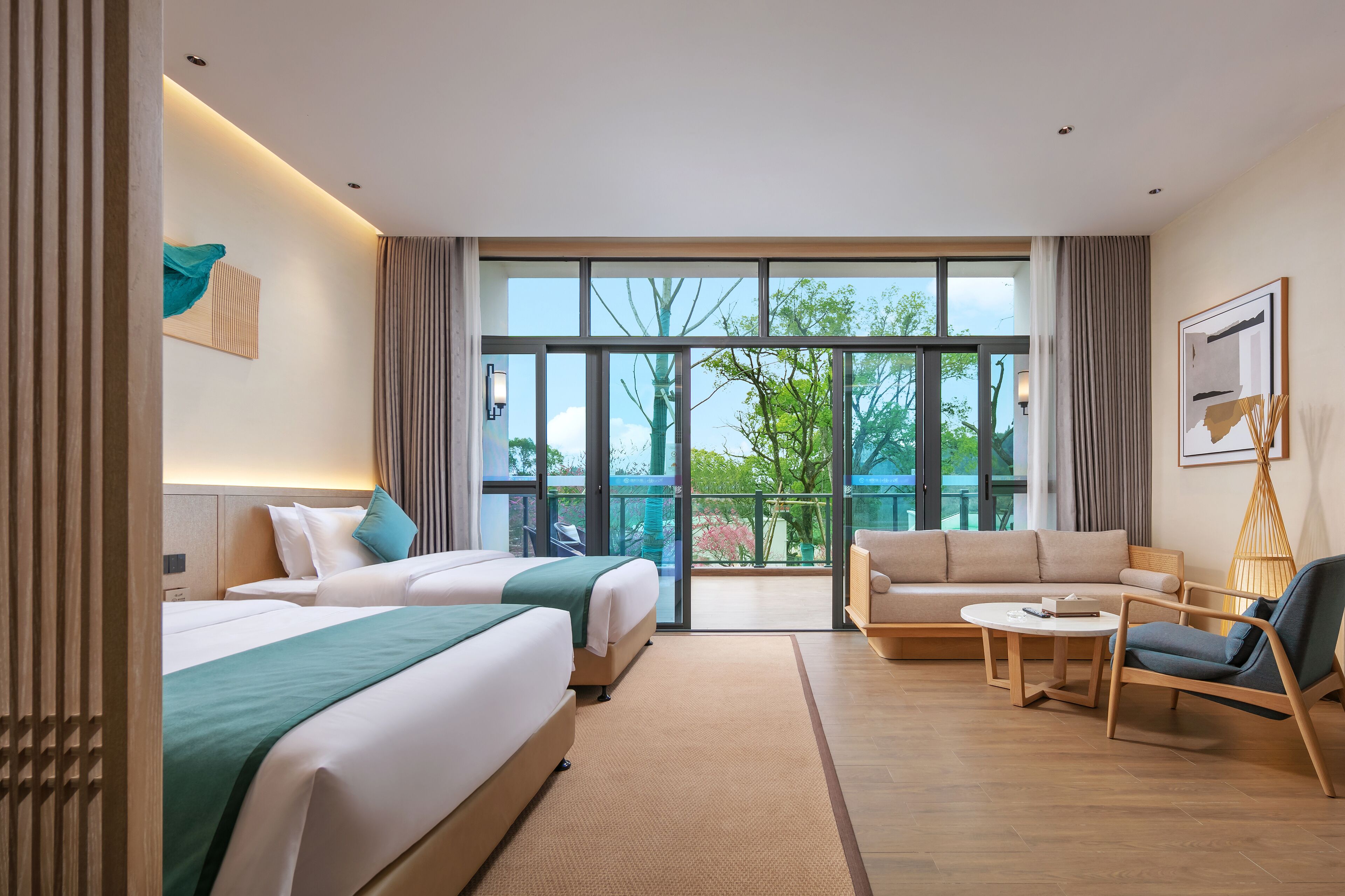 Habitación de hotel con dos camas, un sofá, una mesita y un balcón con vistas a zonas verdes.