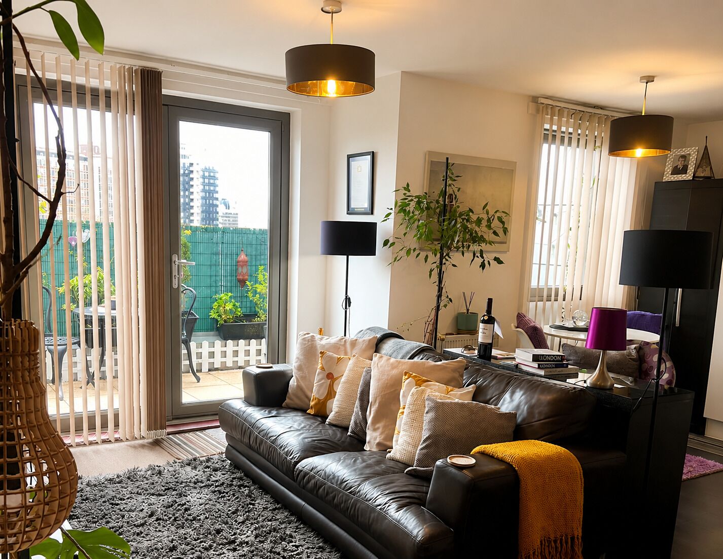 Een moderne woonkamer met een leren bank, zwarte lampen en een uitzicht op een stadsgezicht door grote ramen.