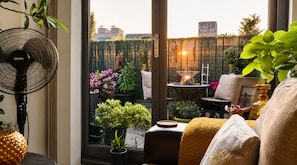 A room with a large window, a fan, and various potted plants.