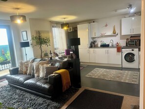 Uma sala de estar moderna com um sofá de couro preto, uma mesa de centro e uma área de jantar ao fundo.