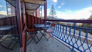 A balcony with a table and chairs, a blue railing, and a view of mountains and trees. - Charming 2-room apartment for 4 in Arc 1800 (Les Arcs 1800)