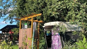 Un giardino con un pergolato in legno, una zona riparata e diverse piante in vaso.