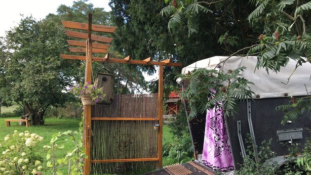 Un giardino con una pergola in legno, una panchina, piante in vaso e una zona riparata con una tenda viola.