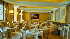 Une salle à manger élégante, dotée de plusieurs tables et chaises, d’un tableau central et de panneaux décoratifs sur les murs.
